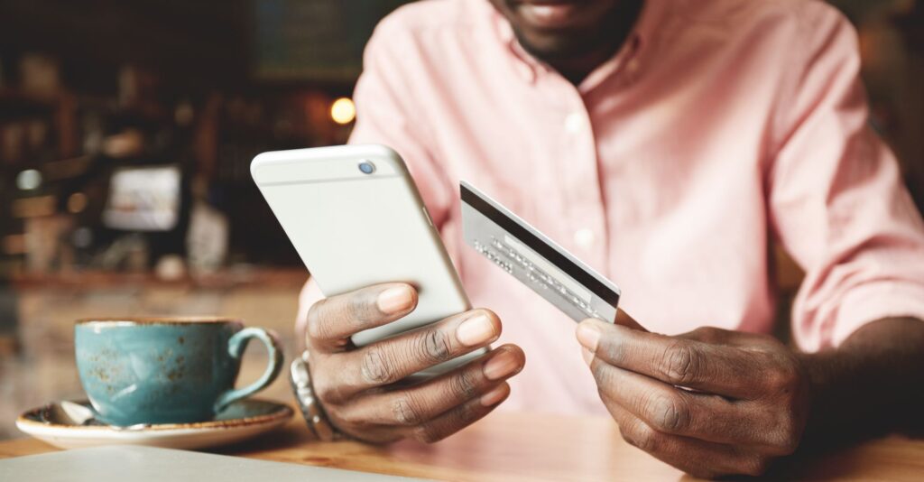 Mãos masculinas segurando celular e cartão de crédito para fazer cálculo dos juros compostos