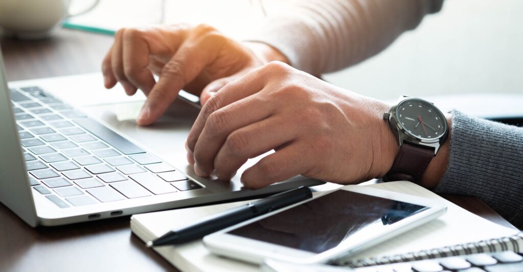 Mãos masculinas pesquisando no teclado do laptop sobre como atrair clientes nas redes sociais