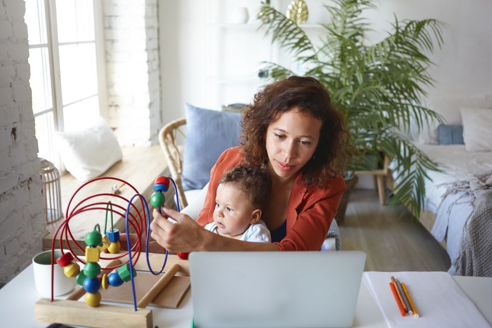 Mulher com bebê no colo em frente ao laptop ilustrando retorno das gestantes ao trabalho